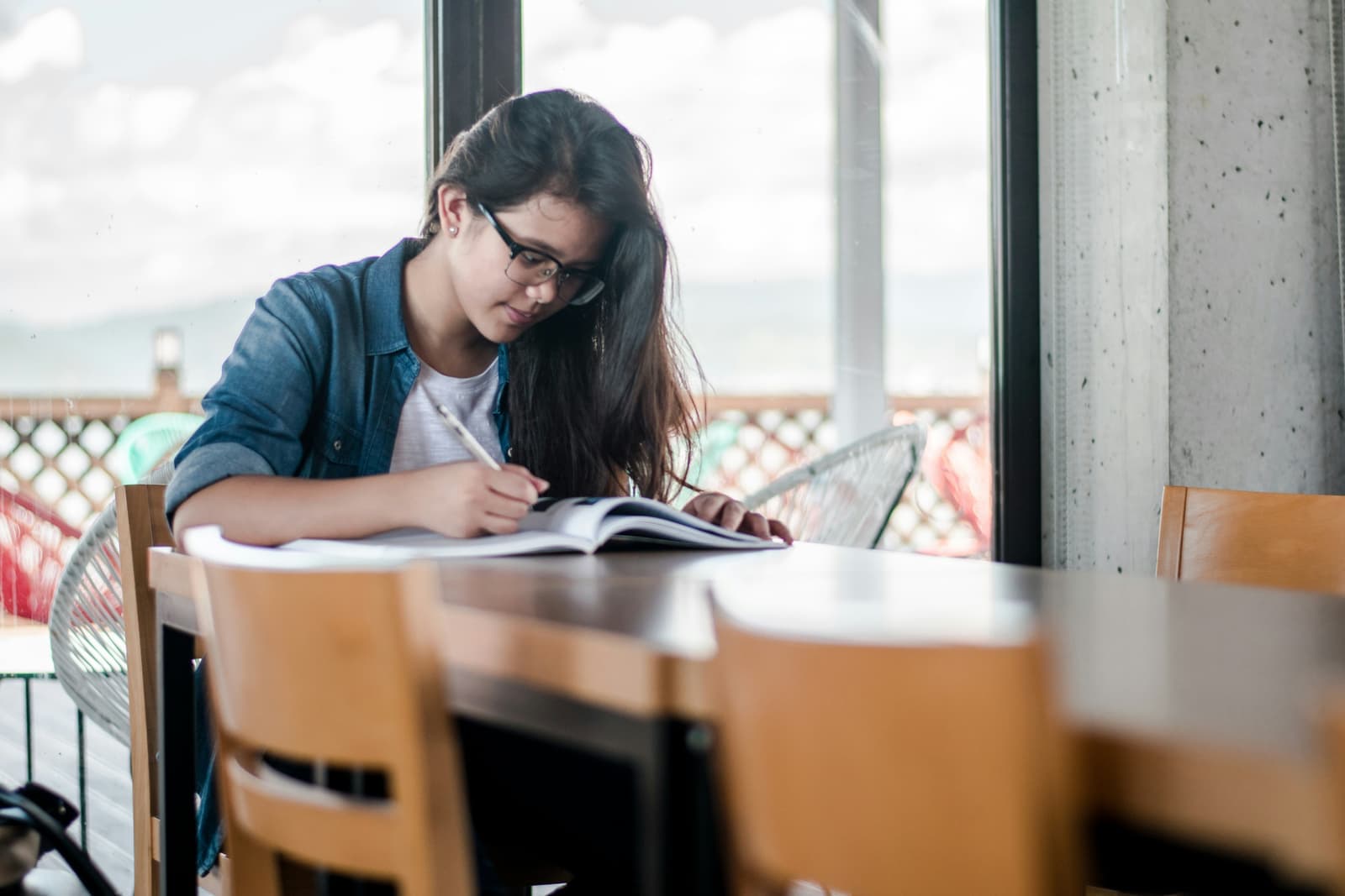 A student writing in a workbook at a table beside a large window while preparing for Essential Digital Skills Level 1