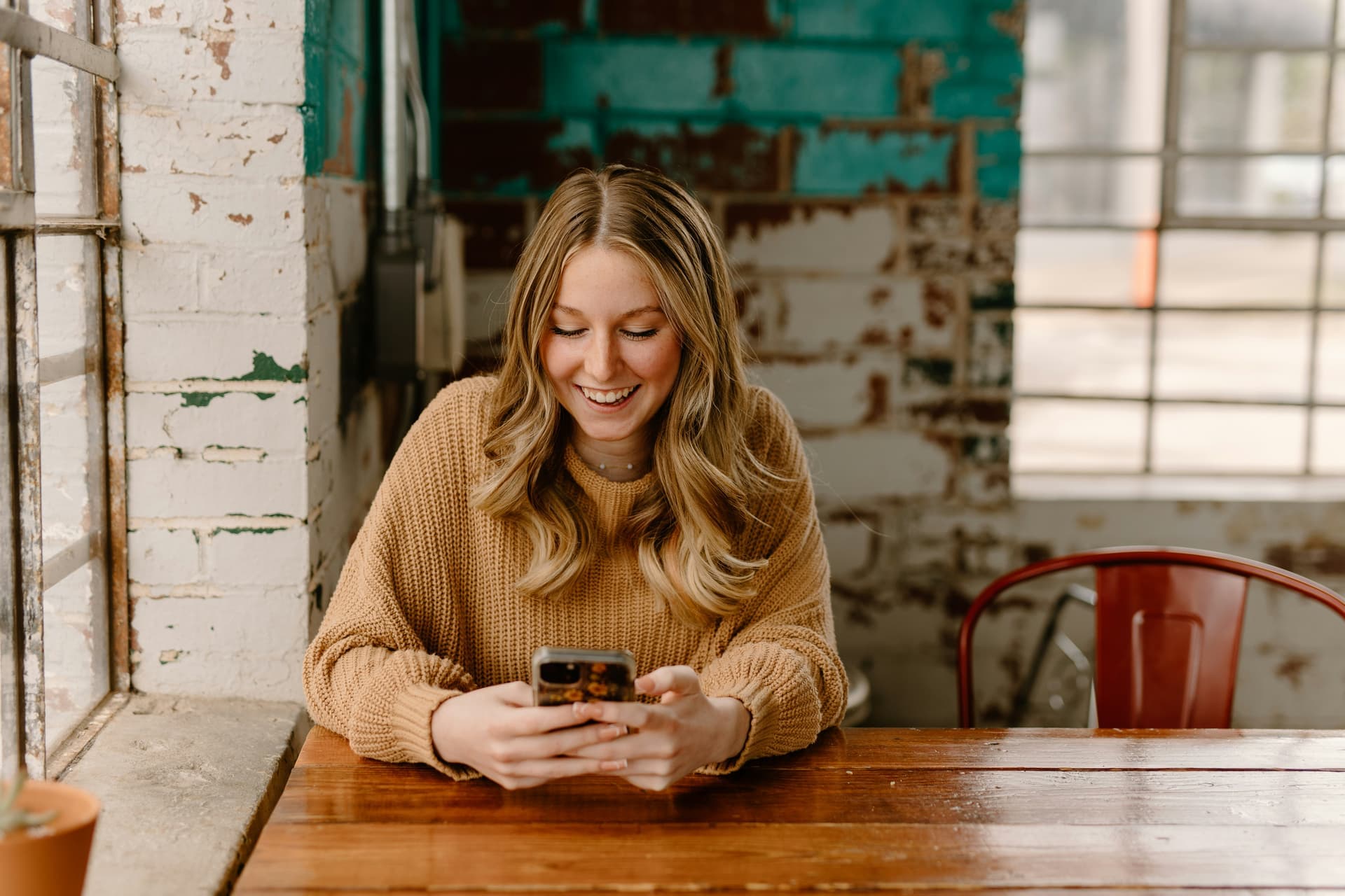 A young woman smiling while using her smartphone in a casual workspace