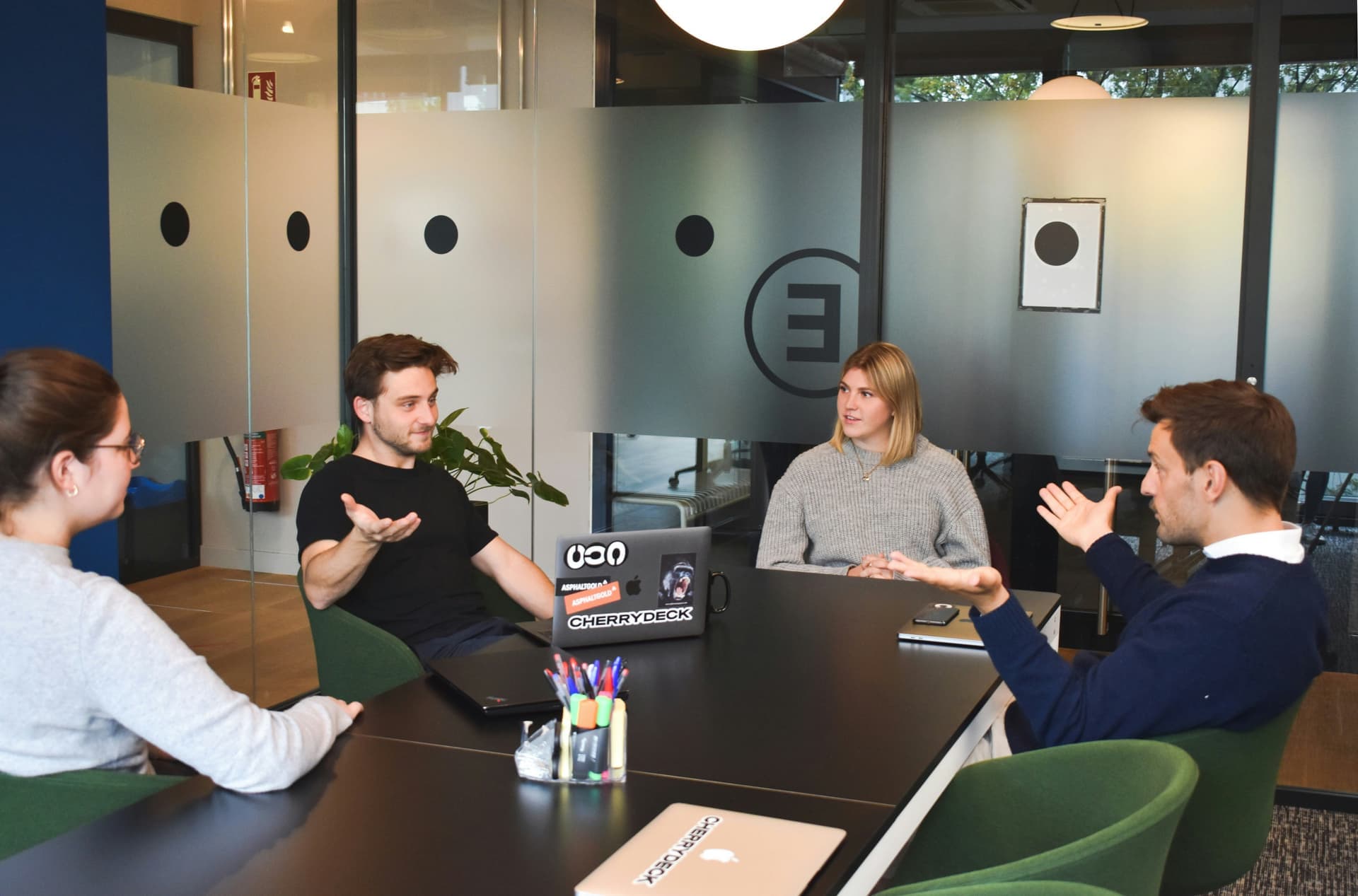 A team of colleagues discussing around a table in a modern glass-walled office