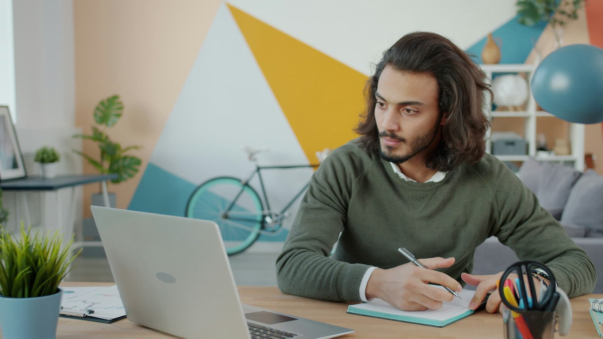 An adult learner taking notes while studying at a laptop